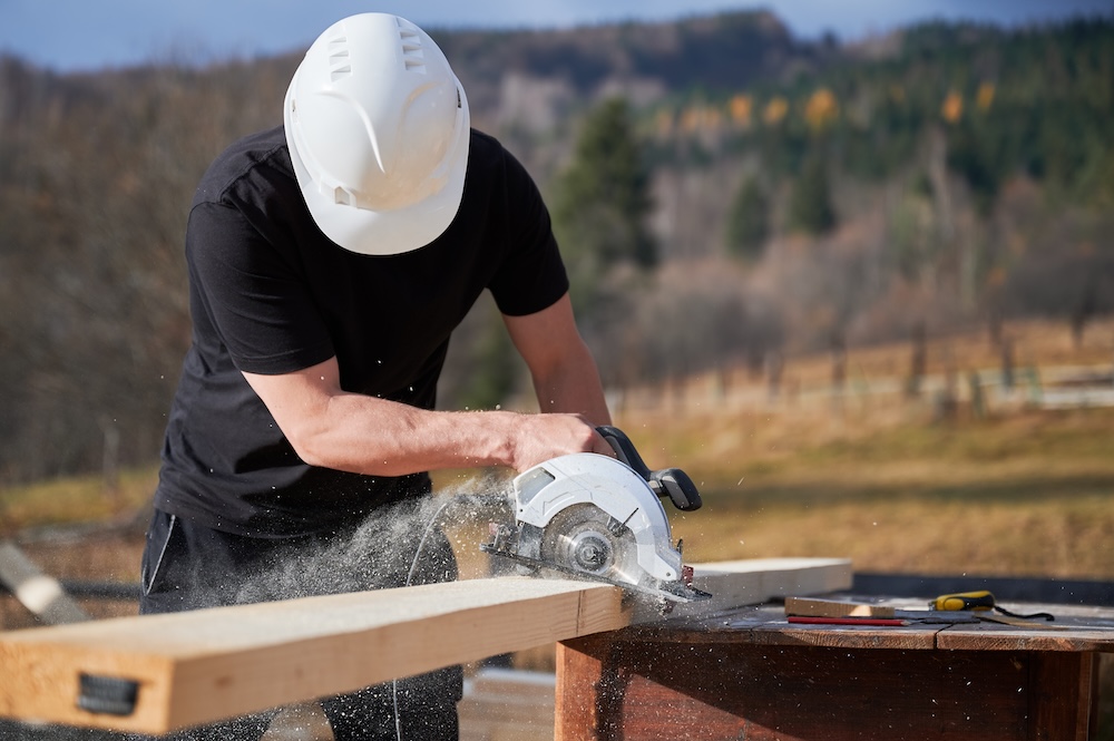 pracownik w kasku tnący deski 